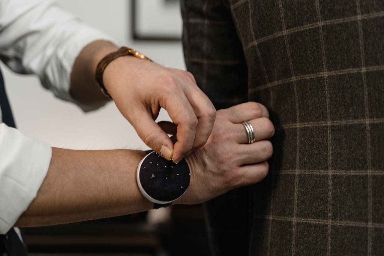 about-us Close-up of a tailor adjusting a checkered suit jacket during a fitting session.